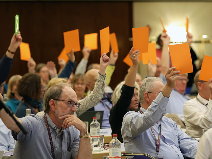 Menschen heben Abstimmkarten bei einer Synode möglicherweise bei einer Abstimmung zum Thema Klimagerechtigkeit.