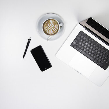 Arbeitstisch von oben mit Laptop, Kaffeetasse, Smartphone und Stift.