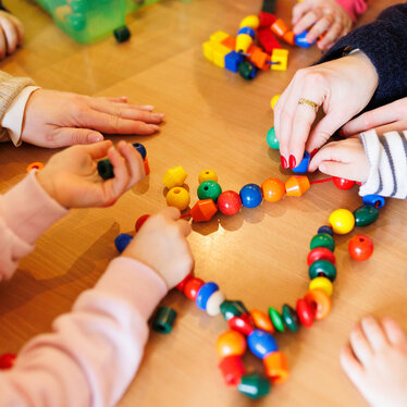 Kinderhände in einer Kita legen gemeinsam eine Reihe aus Kugeln. Ein gutes Beispiel für Bildungsangebote für Kinder in Kita und Gemeinde.