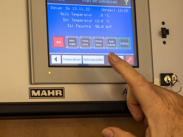 Energiesparen in der Kirche. In der Nazarethkirche in Frankfurt Eckenheim wird die Temperatur des Kircheninnenraumes über ein Thermometer gemessen und und die moderne Heizung lässt sich über ein Display steuern. Im Bild ist das Display zu sehen und eine Hand, die mit einem Finger auf die Tasten deutet.